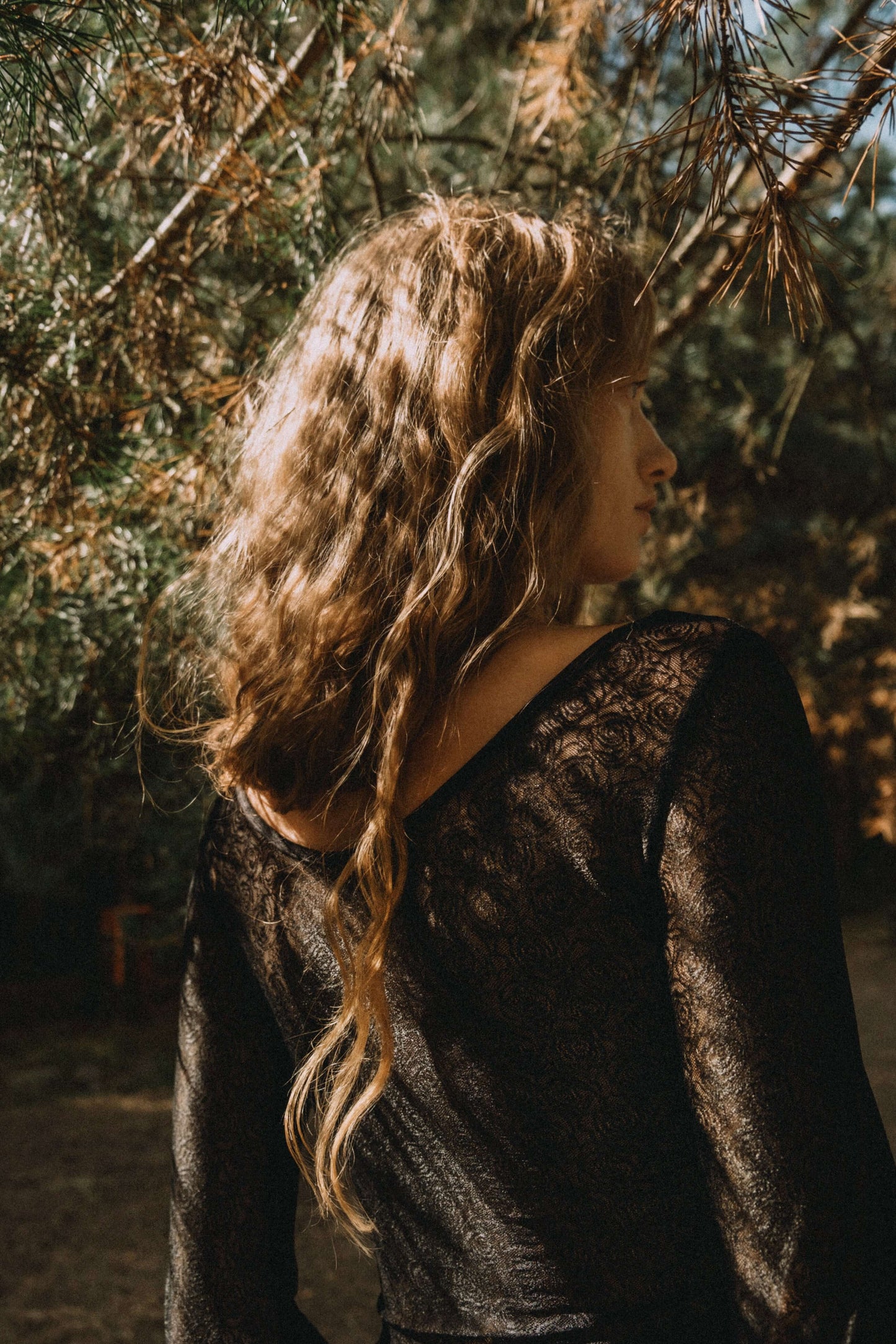 Model wearing a black lace body with floral pattern, showing a profile view in a natural outdoor setting.
