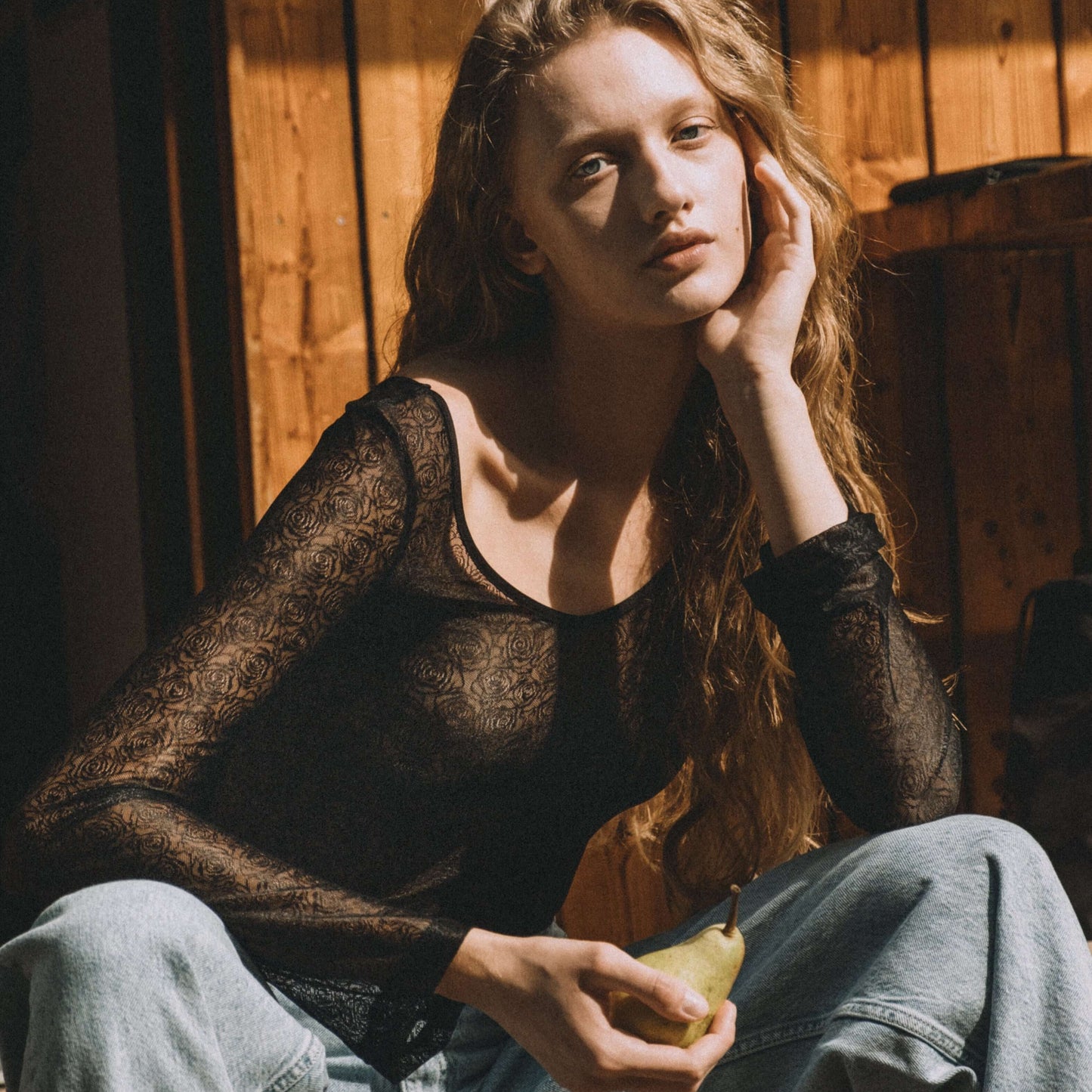 Woman in black lace body Diana top, sitting casually with a pear, showcasing its elegant design.