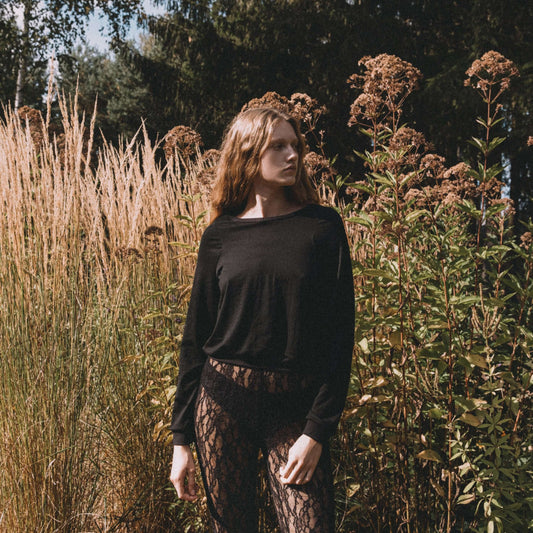 Model in a black top and patterned leggings among tall grass and plants in a natural setting.